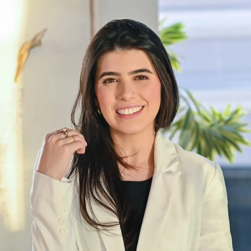 Advogada do escritório, de blazer claro, em retrato no ambiente do escritório.